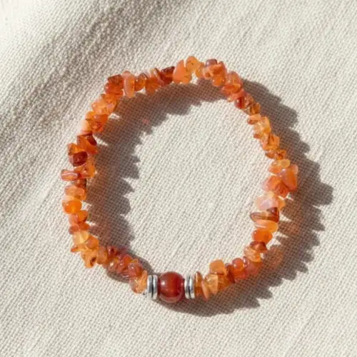 Natural Carnelian Crystal Chip Bracelet with Orange Gemstone Beads, Round Carnelian Center Stone and Silver Spacers on Beige Fabric | OneTrend India